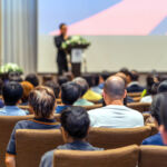 Back side of audience listening the Speaker with podium on the stage in the conference hall, business and education concept